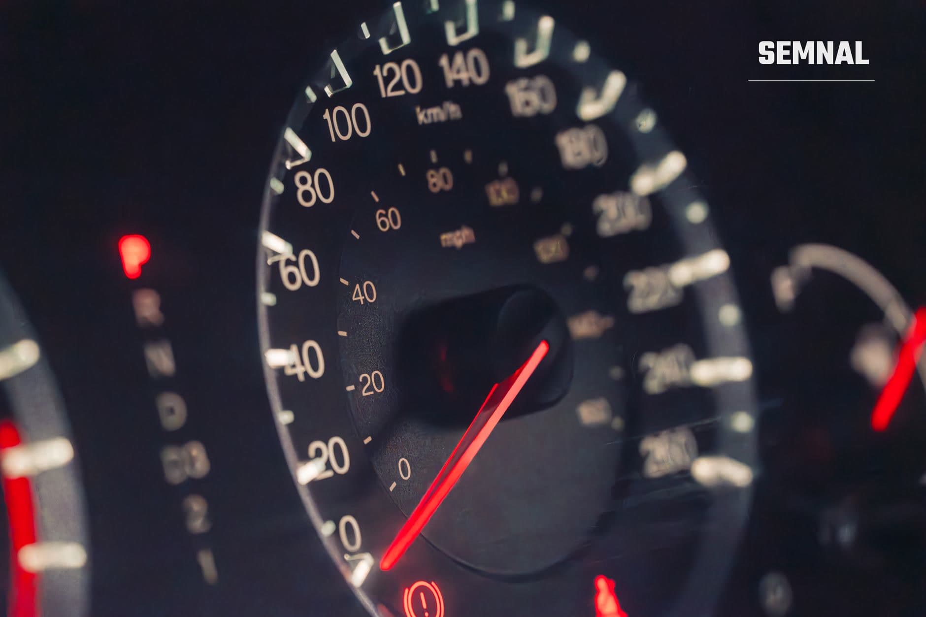 Speedometru de automobil iluminat nocturn cu ac roșu poziționat la aproximativ 20 km/h și scale de viteză în km/h vizibile pe cadranul negru. (Foto: Luke Miller / Pexels)